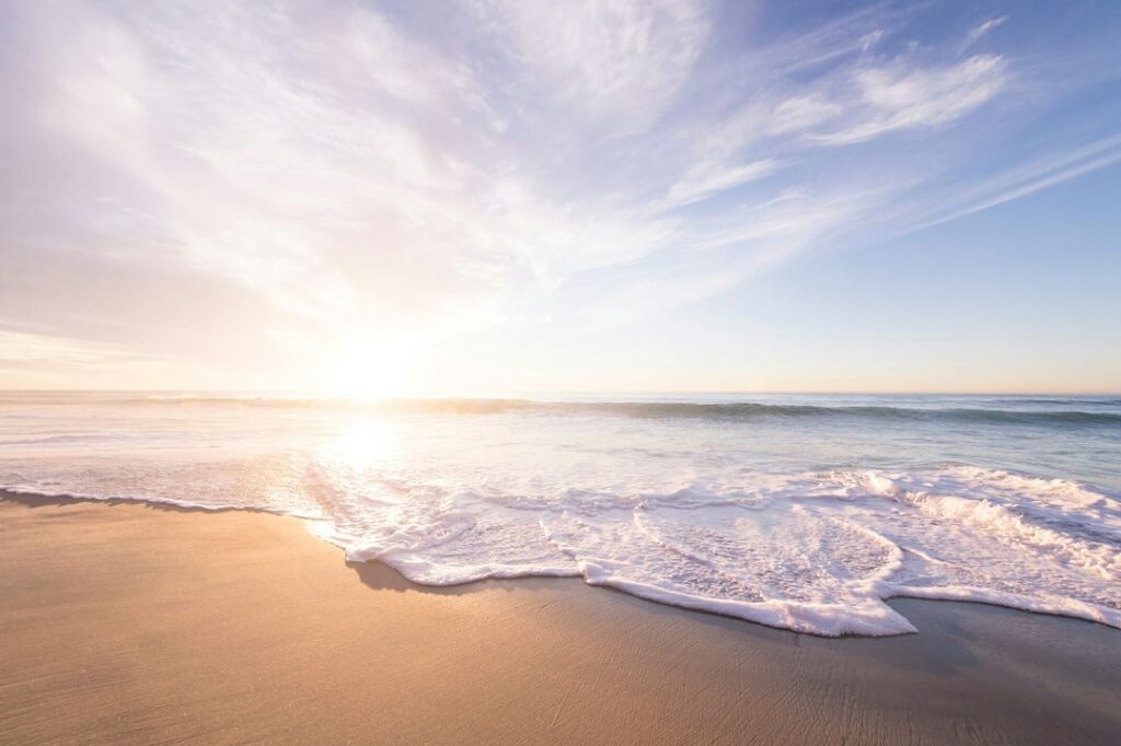 Sunrise over a tranquil beach, with gentle waves lapping the sandy shore and soft morning light illuminating the sky.